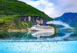 A large passenger ferry with a red hull and white multi-deck superstructure sails across calm blue water, leaving a white wake behind.