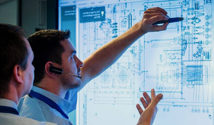 Two people reviewing and pointing at technical engineering drawings displayed on a large digital screen