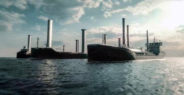 Large vessel at sea fitted with multiple vertical wind-assisted propulsion sails, viewed from the water under a cloudy sky.