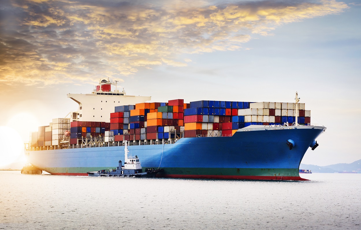 An image of large container ship sailing to harbour with a tugboat nearby